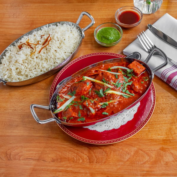 Chicken tikka masala and basmati rice in metal serving dishes on a wooden table.