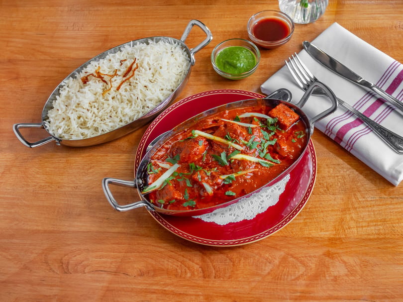 Chicken tikka masala and basmati rice in metal serving dishes on a wooden table.