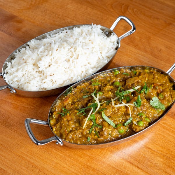 Two silver bowls on a wooden table, one with white rice and the other with curry.