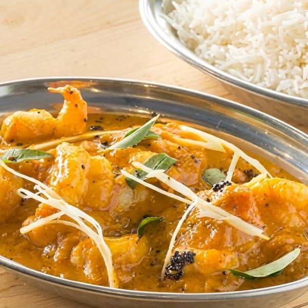 Shrimp curry in a silver bowl, garnished with ginger and herbs, with a side of white rice.