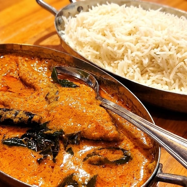 Two metal bowls of Indian food, one with orange curry and the other with white rice.