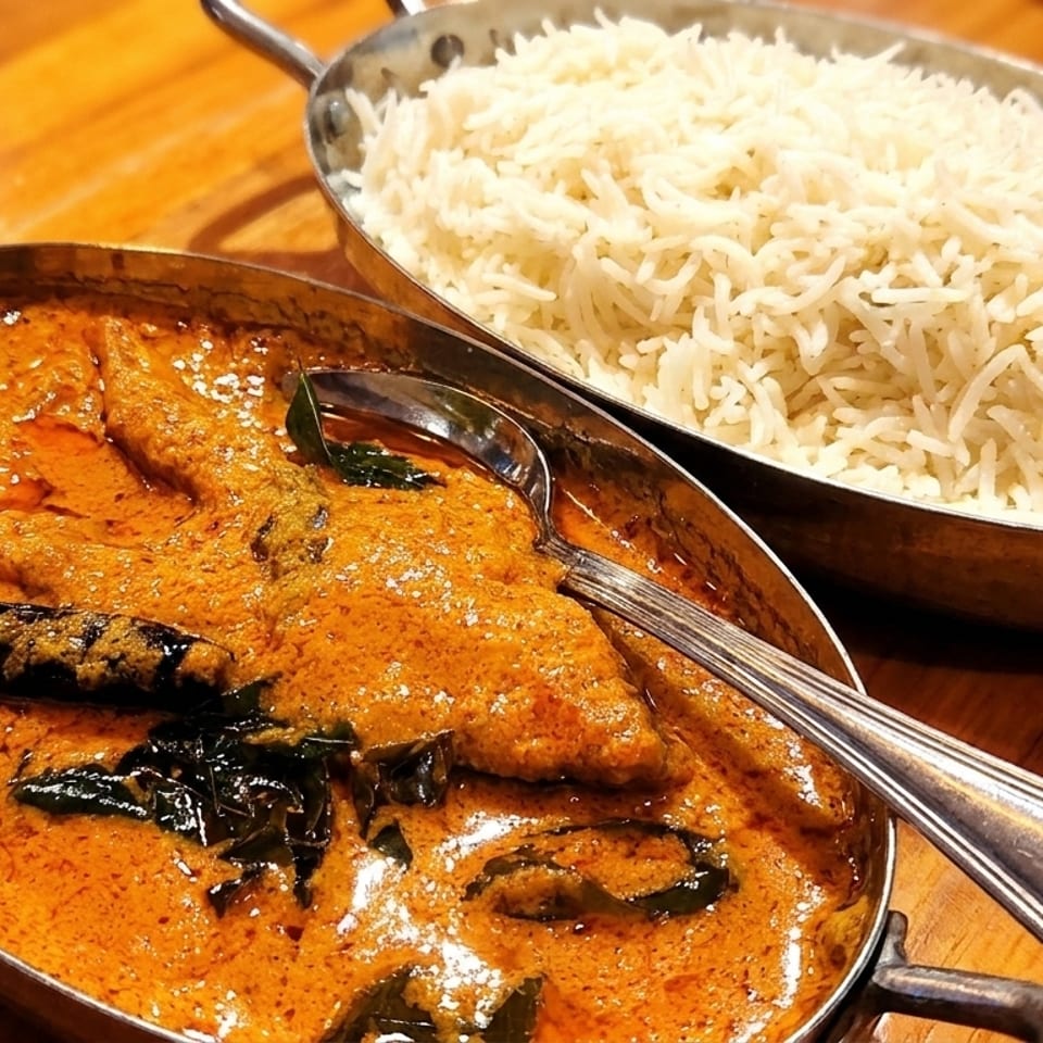 Two metal bowls of Indian food, one with orange curry and the other with white rice.
