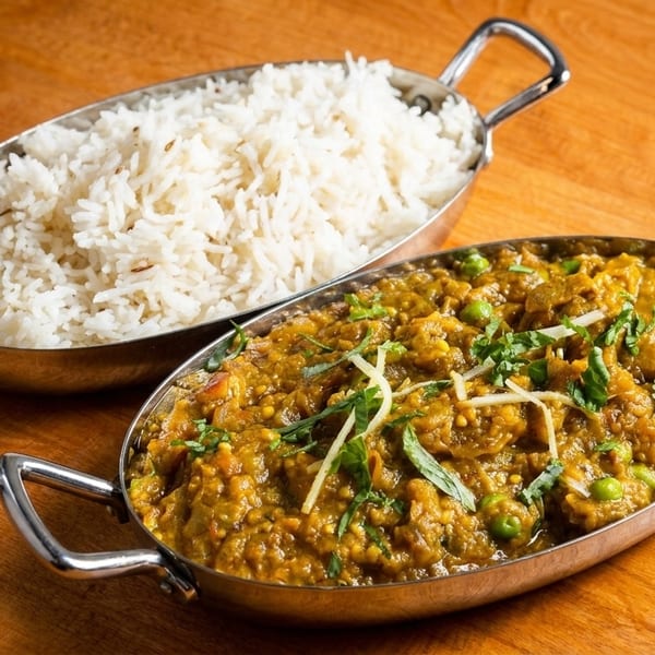 Two metal bowls on a wooden table, one with white rice, the other with green curry.