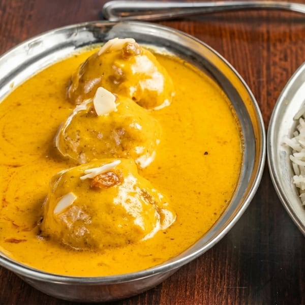 Three malai kofta balls in a rich yellow curry sauce, served with a side of white rice.