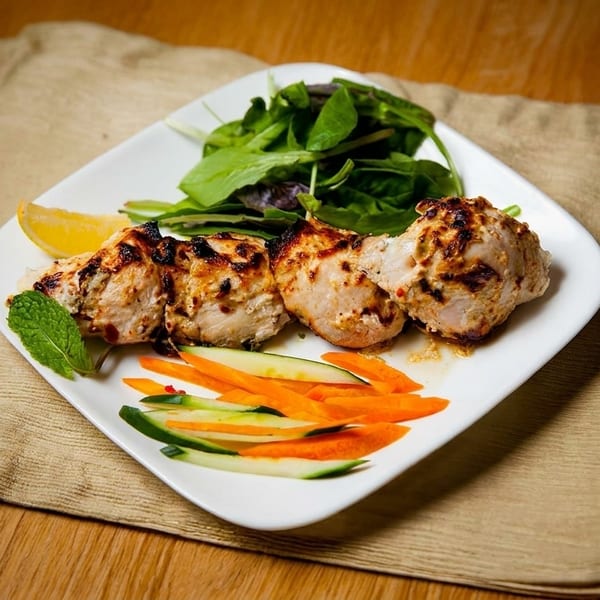 Grilled chicken pieces with a side of fresh green salad, lemon, and julienned carrots and cucumbers.