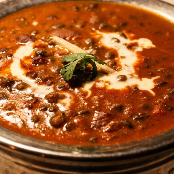 Close-up of a bowl of dal makhani, garnished with cream, cilantro, and ginger.