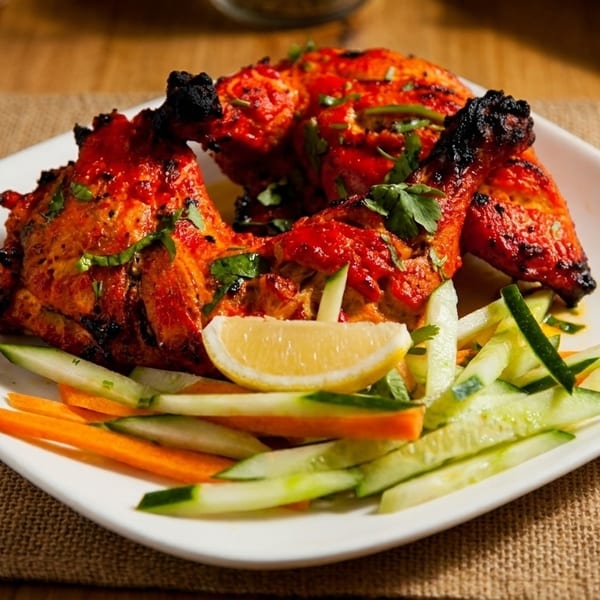 Spicy tandoori chicken with cilantro, lemon, and julienned cucumbers and carrots on a white plate.