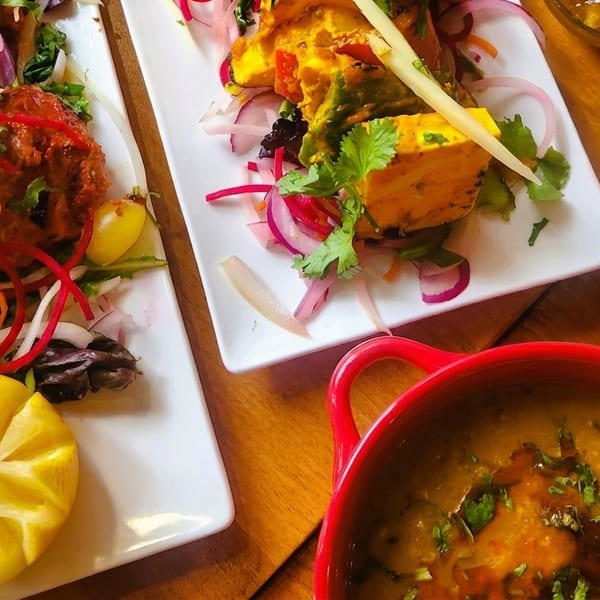Plates of Indian food, including chicken tikka, paneer, dal, and mango chutney on a wooden table.