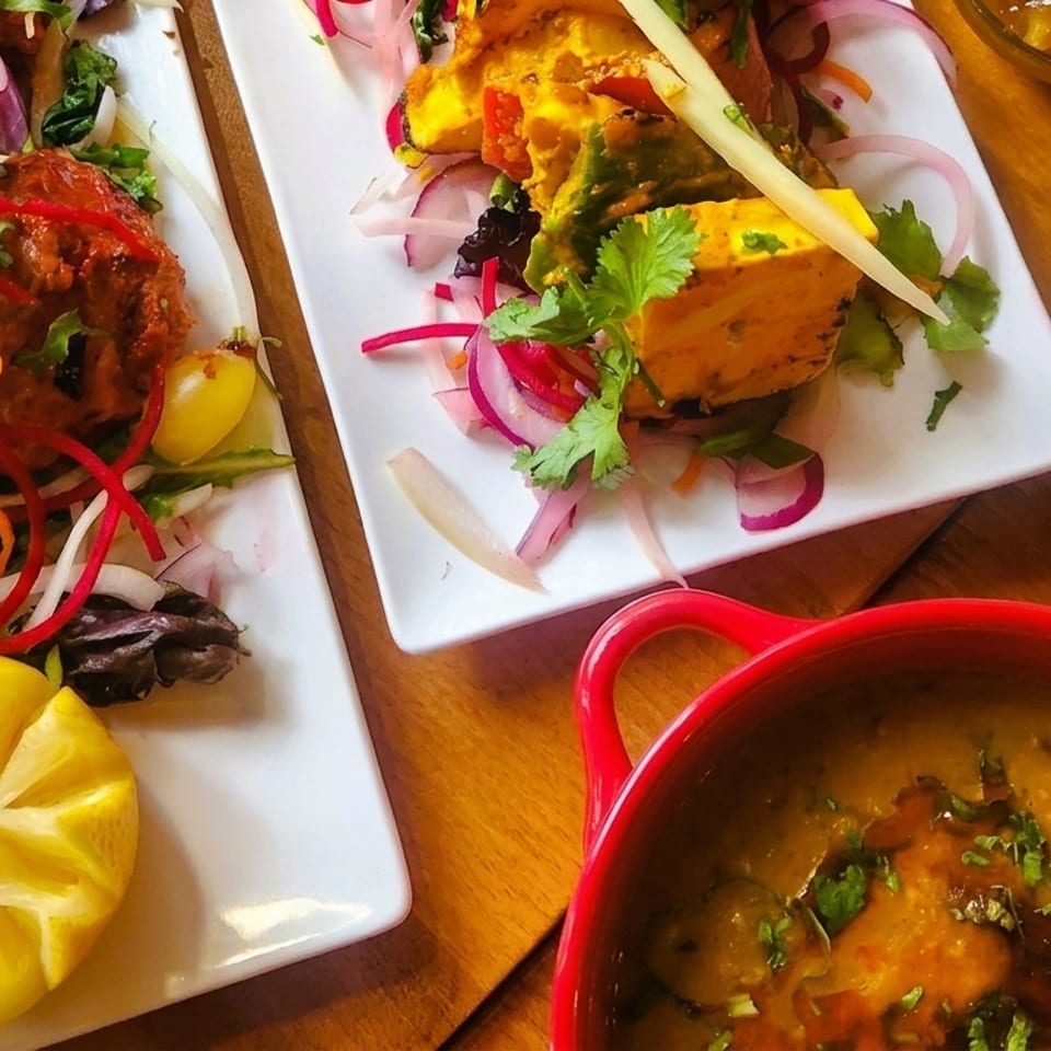 Plates of Indian food, including chicken tikka, paneer, dal, and mango chutney on a wooden table.