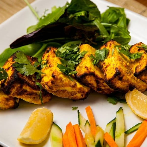 Grilled paneer cheese cubes with cilantro, a side salad, lemon, carrots, and cucumbers.