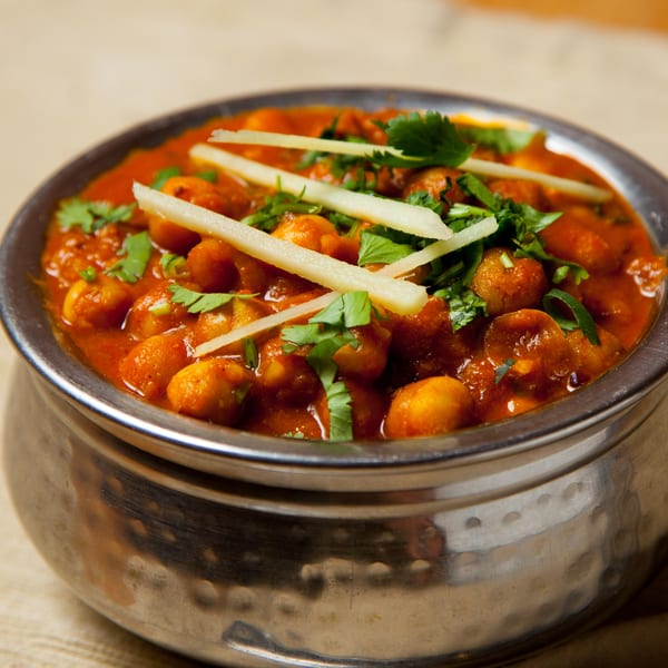 A metal bowl filled with chana masala, garnished with fresh cilantro and ginger slivers.