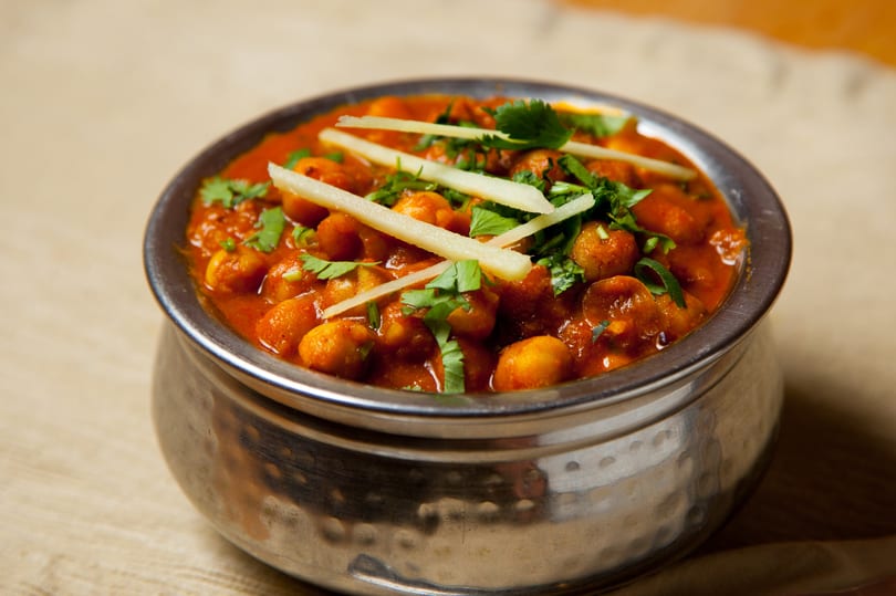 A metal bowl filled with chana masala, garnished with fresh cilantro and ginger slivers.